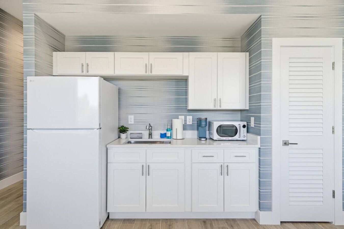 A compact kitchen with white cabinets, a refrigerator, a microwave, and a sink.