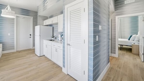 Une cuisine moderne avec des meubles blancs, un réfrigérateur et un évier. Le sol est en bois et il y a un luminaire au plafond.