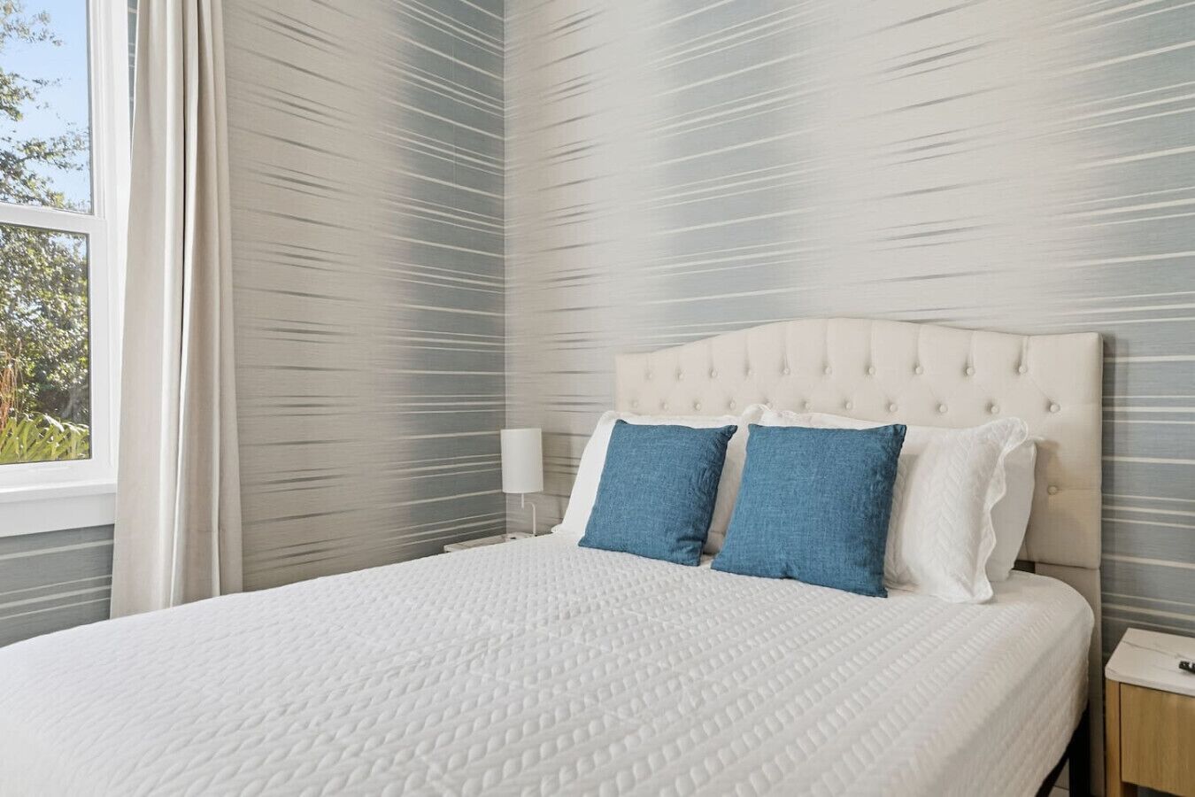 Un lit bien fait, recouvert d’une couette blanche, avec deux oreillers bleus et une tête de lit capitonnée.