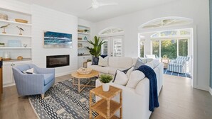 Una sala de estar amplia con chimenea, ventilador de techo y vistas al exterior.