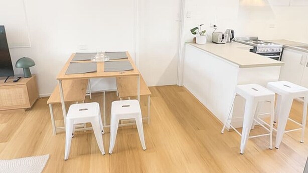 Una cocina moderna con una mesa de madera y taburetes, una encimera blanca y una campana extractora de acero inoxidable.