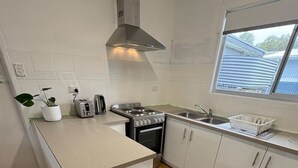 Una cocina moderna con armarios blancos, una campana de acero inoxidable, horno empotrado, un lavamanos y dos taburetes blancos.
