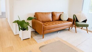 Una sala de estar moderna con un sofá de cuero marrón, un sillón verde y una planta blanca en maceta.