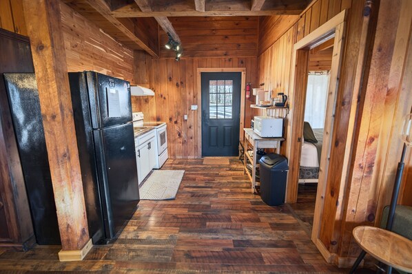 A wooden cabin interior with a black refrigerator, white microwave, and wooden cabinets.
