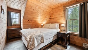 Une chambre à coucher dans une cabane en bois, avec un lit, deux lampes de chevet, une petite table de nuit et une fenêtre avec des rideaux.