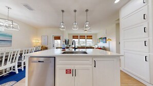 Una cucina moderna con isola centrale, elettrodomestici in acciaio inossidabile, illuminazione a sospensione e vista sull'area pranzo.