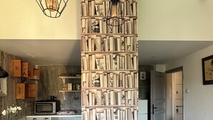 Uma cozinha com uma mesa de madeira, cadeiras, um candeeiro pendente e uma estante cheia de livros.
