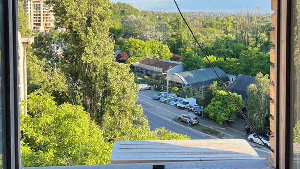 Vista da janela com vista para um parque de estacionamento com carros, um edifício identificado como 