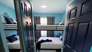 Quarto com beliches, piso de azulejos e porta para outro cômodo.