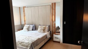 A bedroom with a bed, pillows, a bedside table, and a wooden headboard. - LUXURY POBLADO PARK (Medellín)