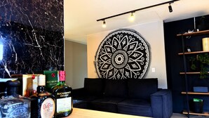 A modern living room with a black couch, a large decorative wall piece, and a shelf with various items including bottles of alcohol. - LUXURY POBLADO PARK (Medellín)