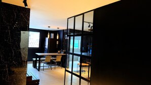 A modern kitchen with a black marble backsplash, a dining area with a wooden table and wicker chairs, and a large window providing natural light. - LUXURY POBLADO PARK (Medellín)