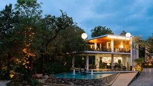 Un edificio moderno con piscina, rodeado de árboles y un sendero bien iluminado.