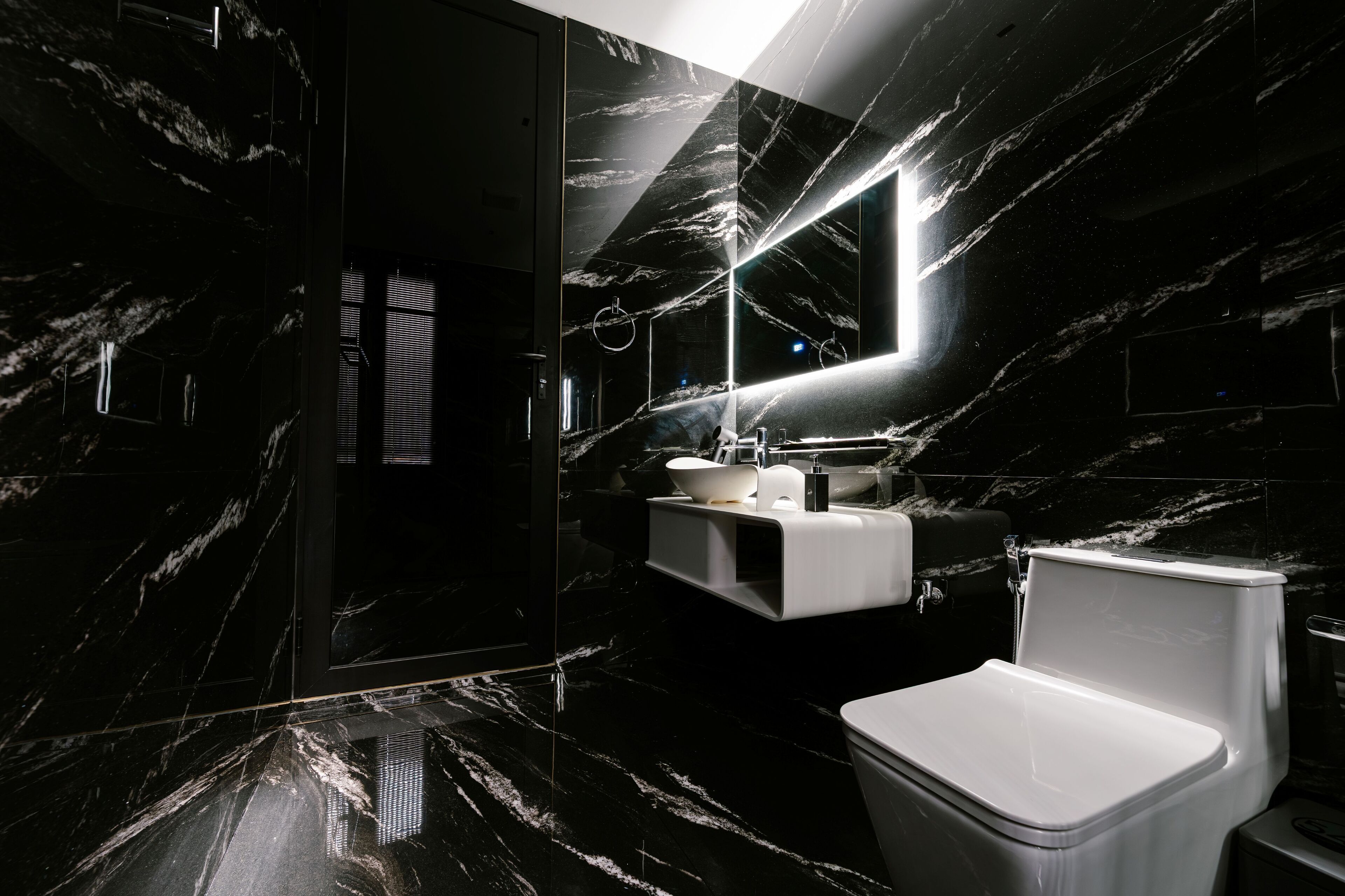 A modern bathroom with a black marble floor, a white sink, and a toilet.