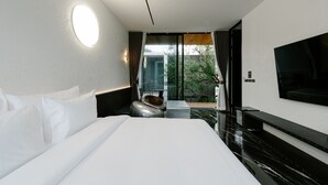 Habitación de hotel moderna con una cama grande, televisor de pantalla plana y balcón con vista a zonas verdes.