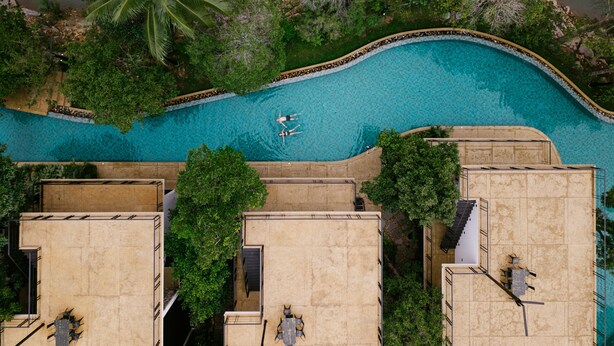 Vista aérea de una piscina rodeada de exuberante vegetación y edificios colindantes.