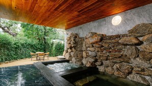 Un espacio de spa con pared de piedra, techo de madera y una zona de estar con sillones.