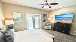 Ein Schlafzimmer mit einem Bett, Deckenventilator, Fernseher, Kommode und einer Tür, die auf einen Balkon führt.