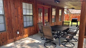 Une terrasse couverte avec une table et des chaises, des murs en bois et un barbecue à l’arrière-plan.