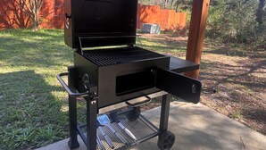Un barbecue portable doté d’une table d’appoint, de roues pour faciliter le déplacement et d’une grille en métal.