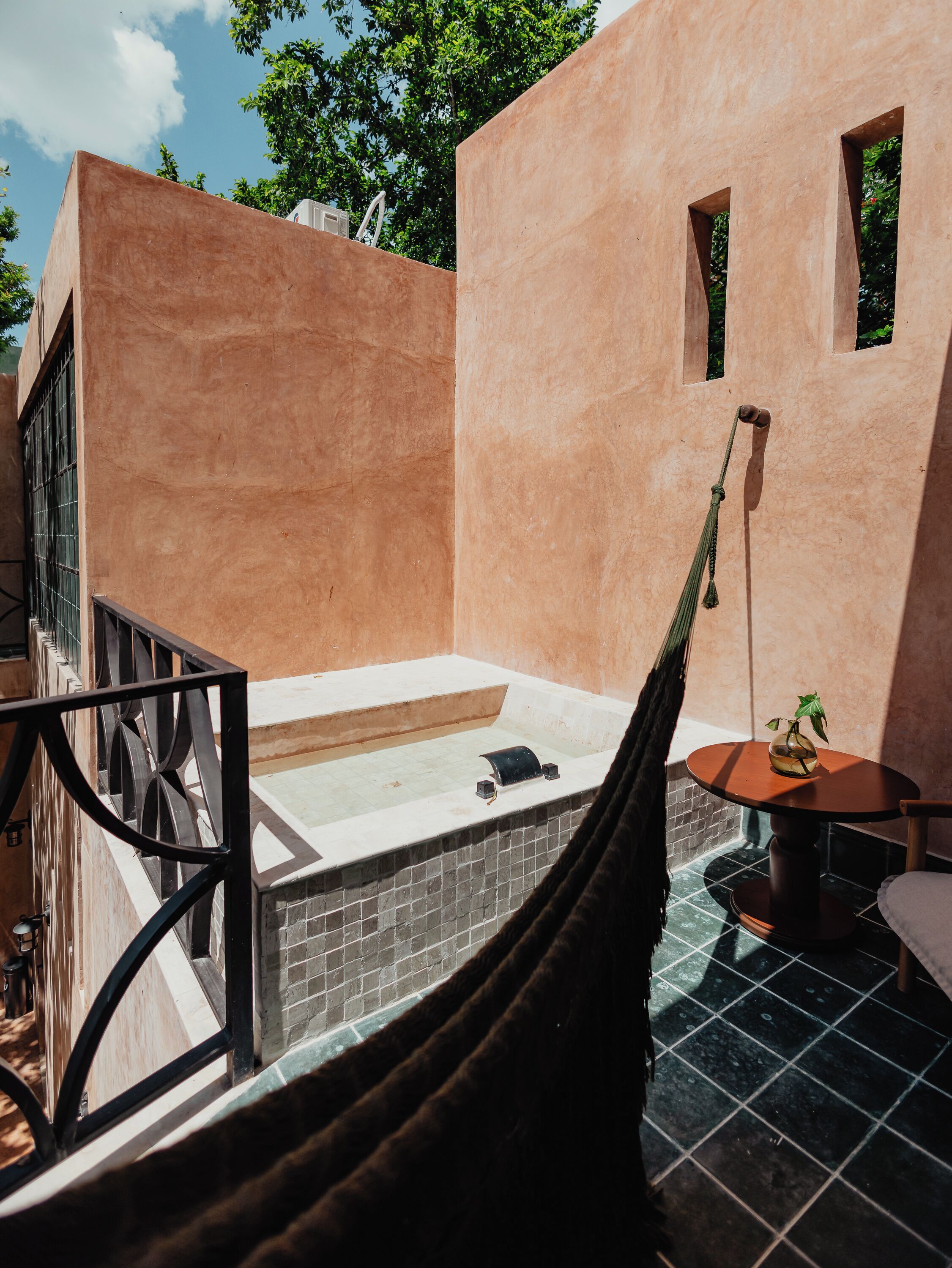 A room with a bathtub, a small table with a plant, and a hammock.