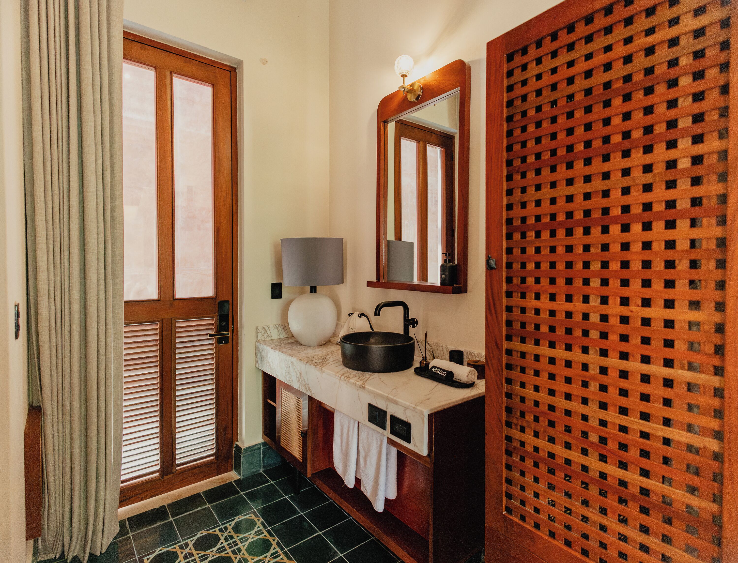 A bathroom with a wooden door, a sink with a mirror above it, a towel rack, and a patterned floor.