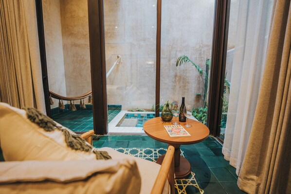 A cozy room with a bed, a small round table with a magazine, and a view of a tiled patio with a pool.