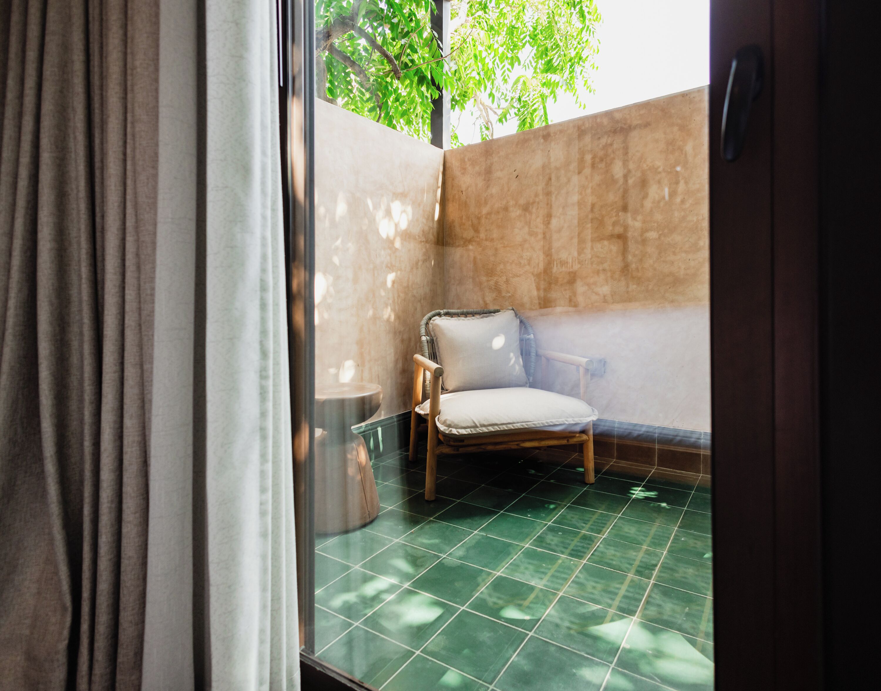 A room with a green tiled floor, a wooden chair with a cushion, and a small round table.