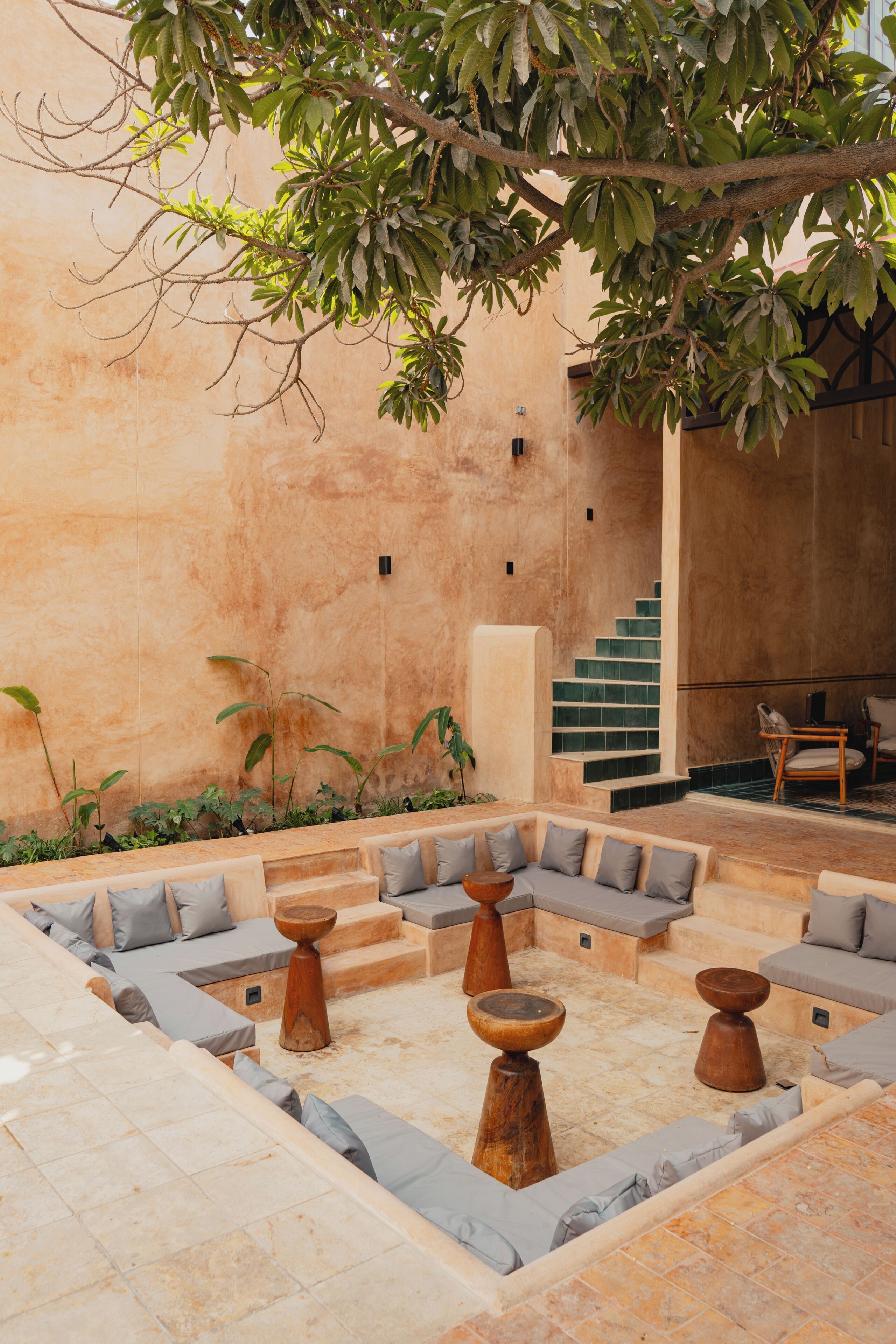 An outdoor seating area with a stone floor, cushioned seating, and wooden tables.