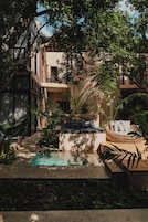 A pool area with a built-in hot tub, surrounded by lush greenery and a multi-level building with balconies.
