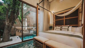 Un dormitorio con una cama grande, un banco, un árbol y vistas a un espacio exterior con piscina.