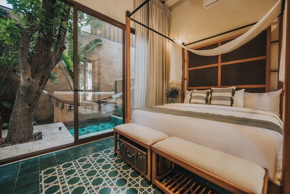 A bedroom with a large bed, a bench, a tree, and a view of an outdoor area with a pool. - CIGNO Mejorada Hotel Boutique (Mérida)