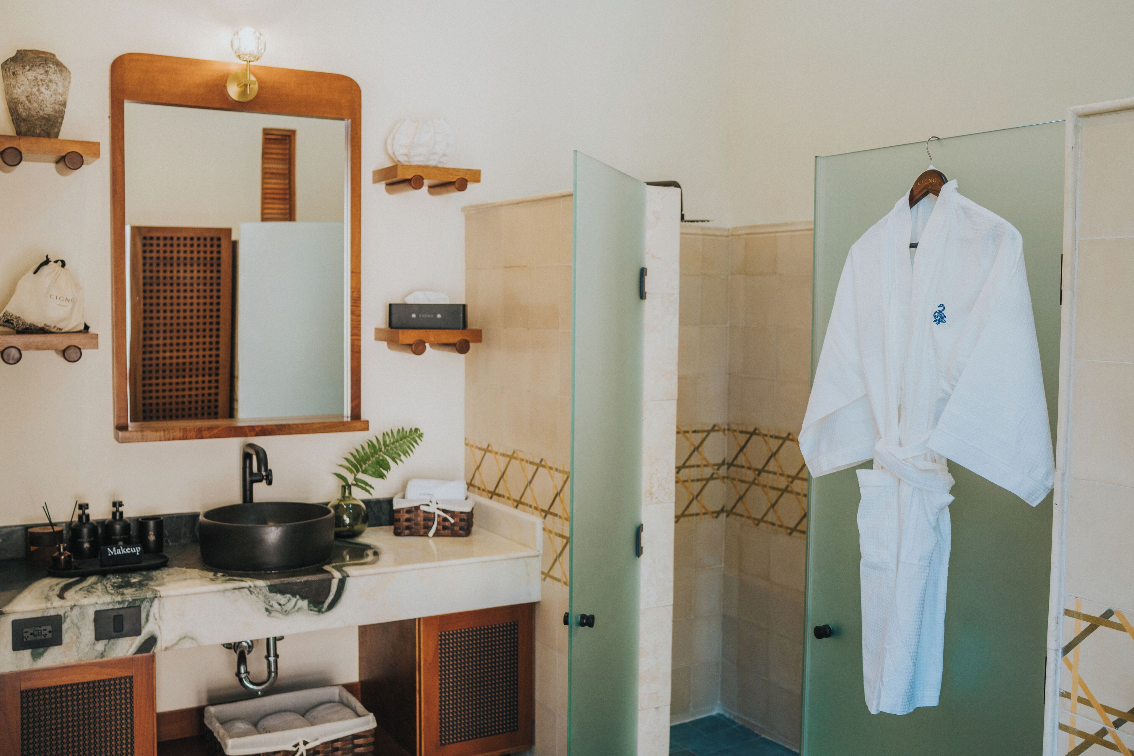 A bathroom with a large mirror, a sink with a black basin, wooden shelves, and a robe hanging on a door.