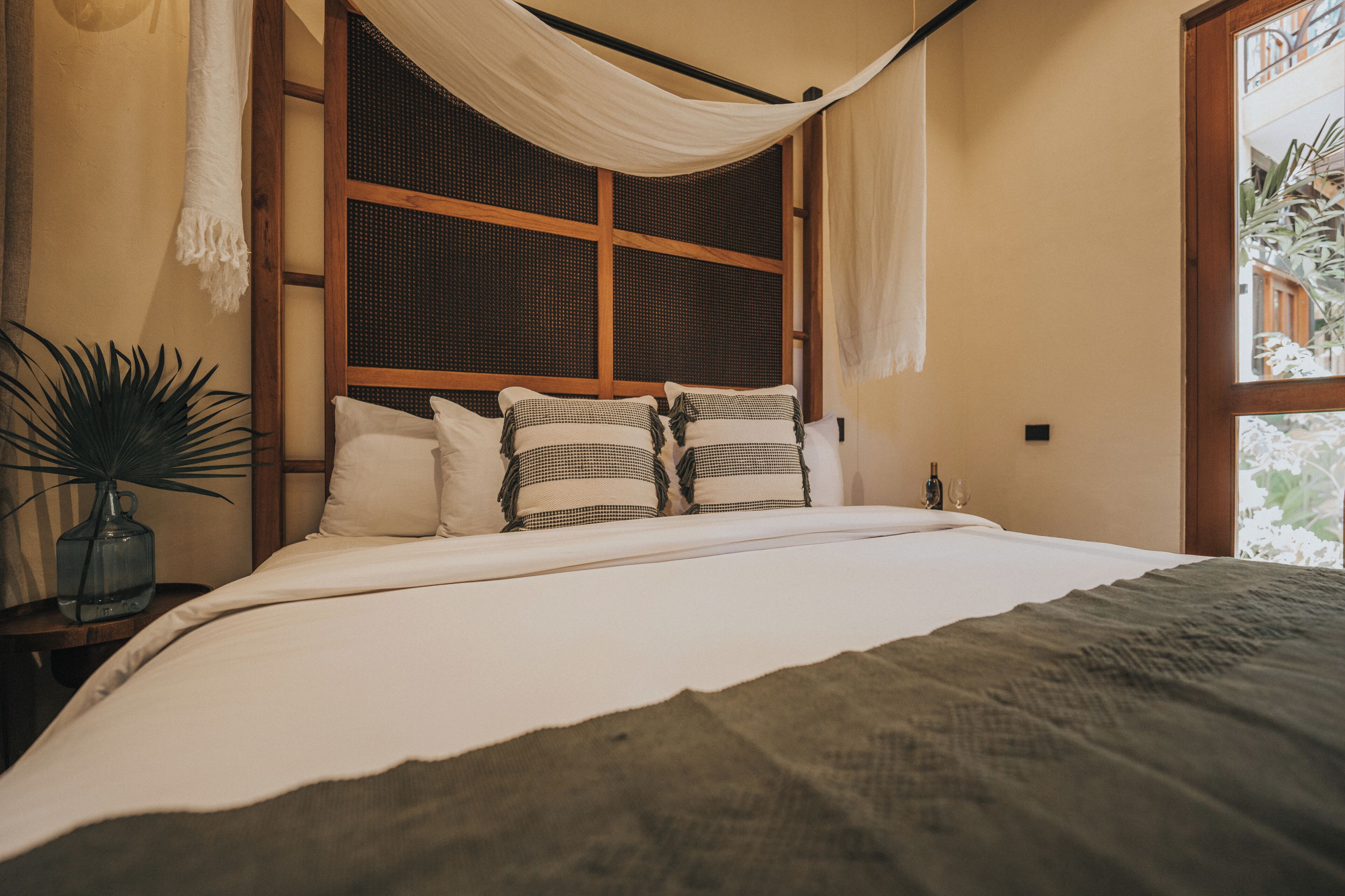 Un dormitorio con una cama grande, un ventanal con vistas y una mesita de noche con una planta.