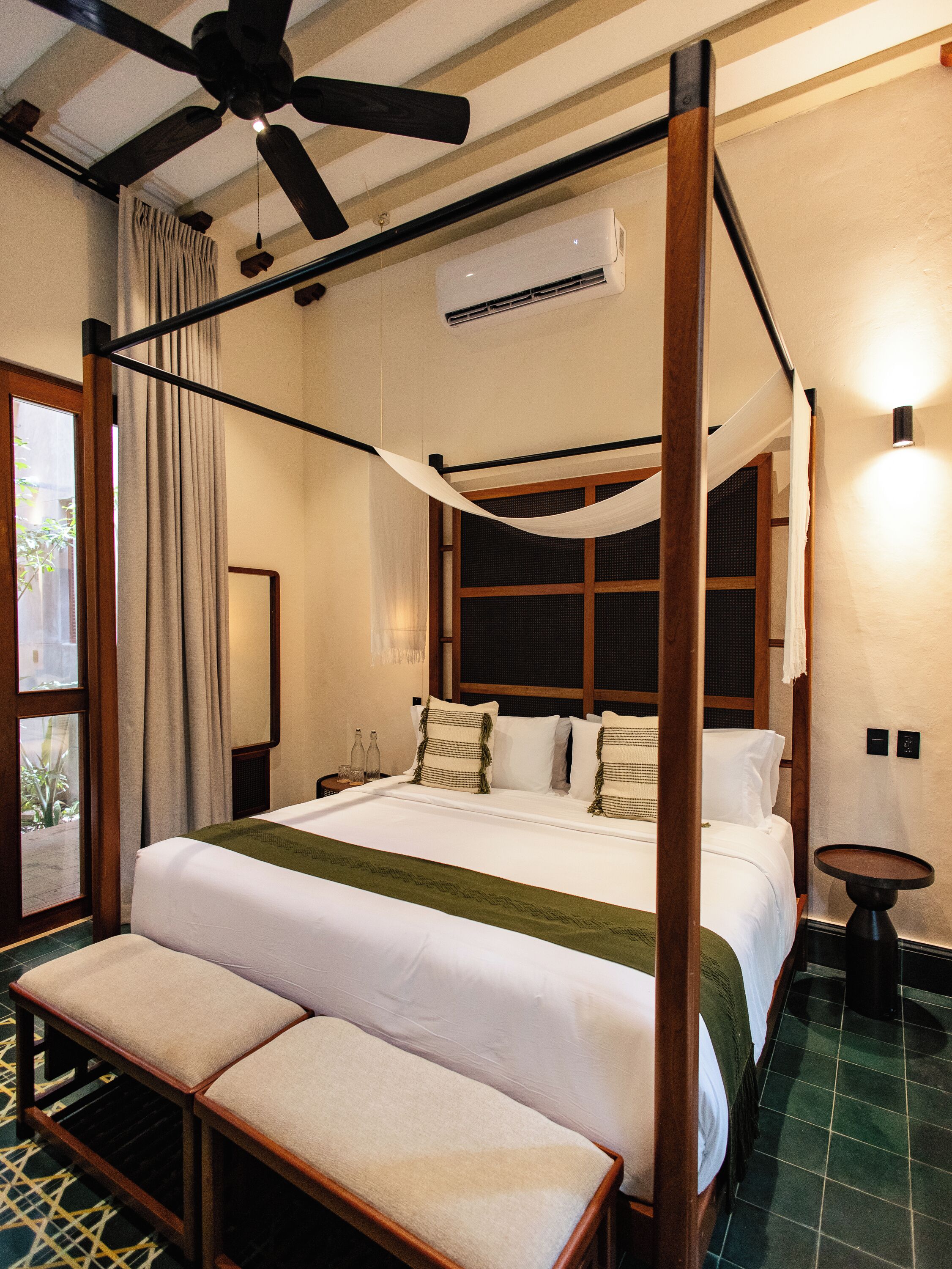 Una cama con dosel, una mesita de noche y una ventana con cortinas.