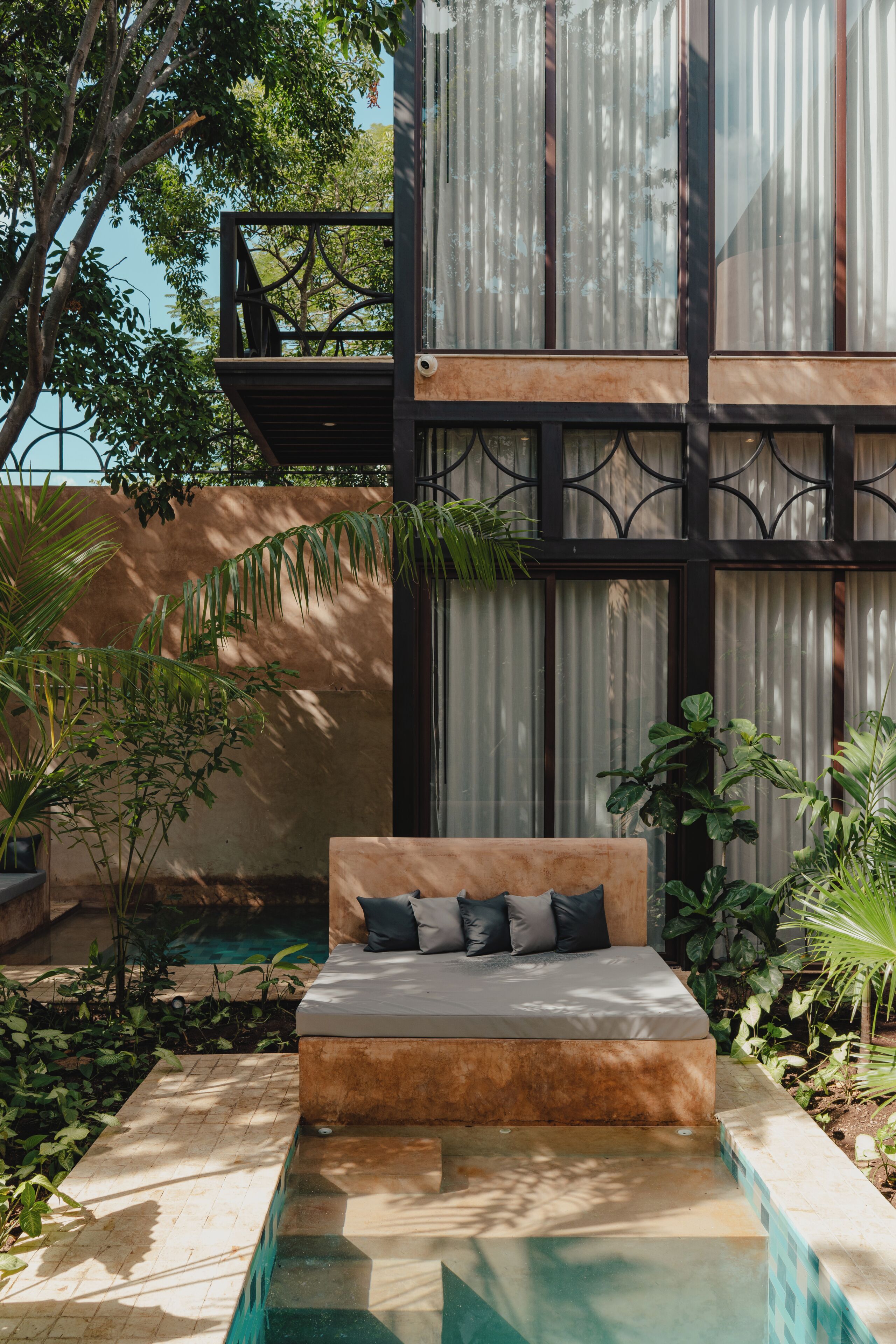 A modern outdoor seating area with a pool, surrounded by lush greenery and a large building with large windows.