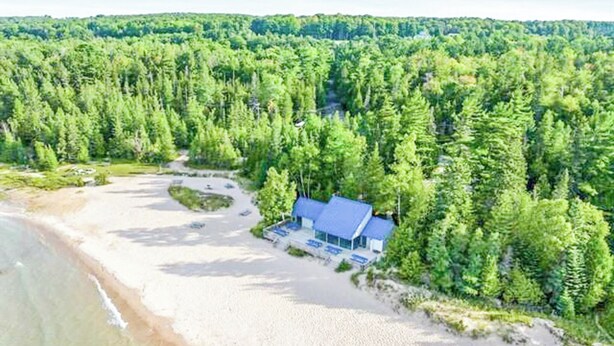 A coastal property with a beach, a small house with a blue roof, surrounded by dense forest. - Harbor Springs Adventure Base—Beach, Trails & Skiing (Harbor Springs)