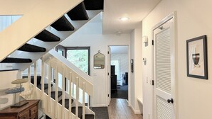 A modern interior with a wooden staircase, a hallway leading to a door, and a framed picture on the wall. - Harbor Springs Adventure Base—Beach, Trails & Skiing (Harbor Springs)