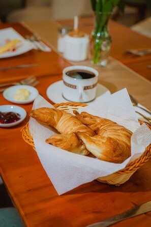 A table with a basket of croissants, a cup of coffee, and small dishes of butter and jam. - HOTEL LA JOYA (Otavalo)