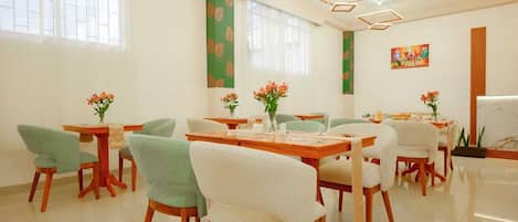 Un espace repas avec plusieurs tables et chaises, un mur d’accent de couleur verte et un tableau accroché au mur.