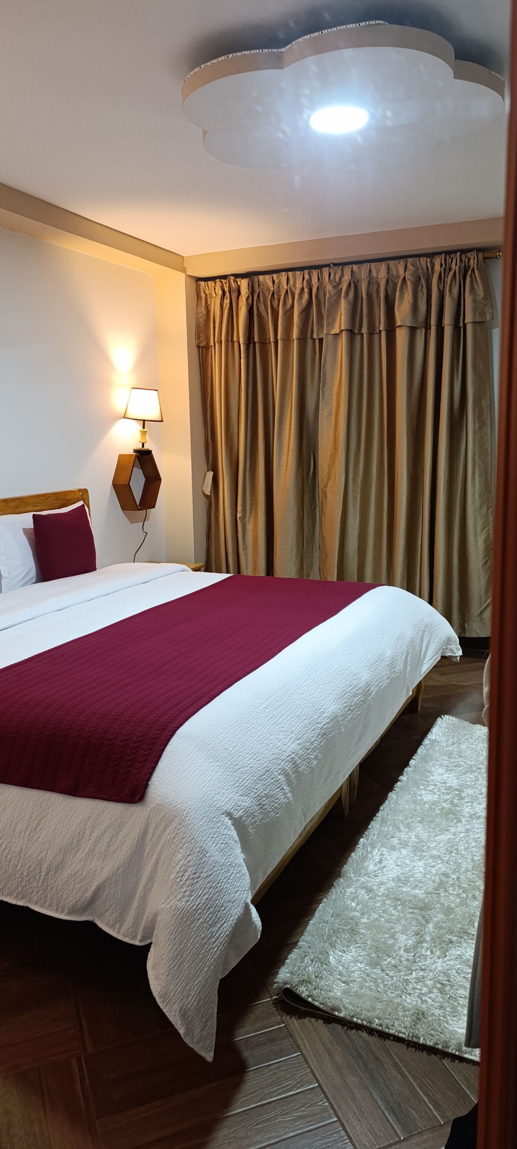 Habitación de hotel con cama, mesita de noche, lámpara y ventana con cortinas.
