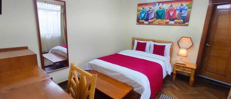 A bedroom with a bed, a desk, a chair, a nightstand with a lamp, and a painting on the wall.
