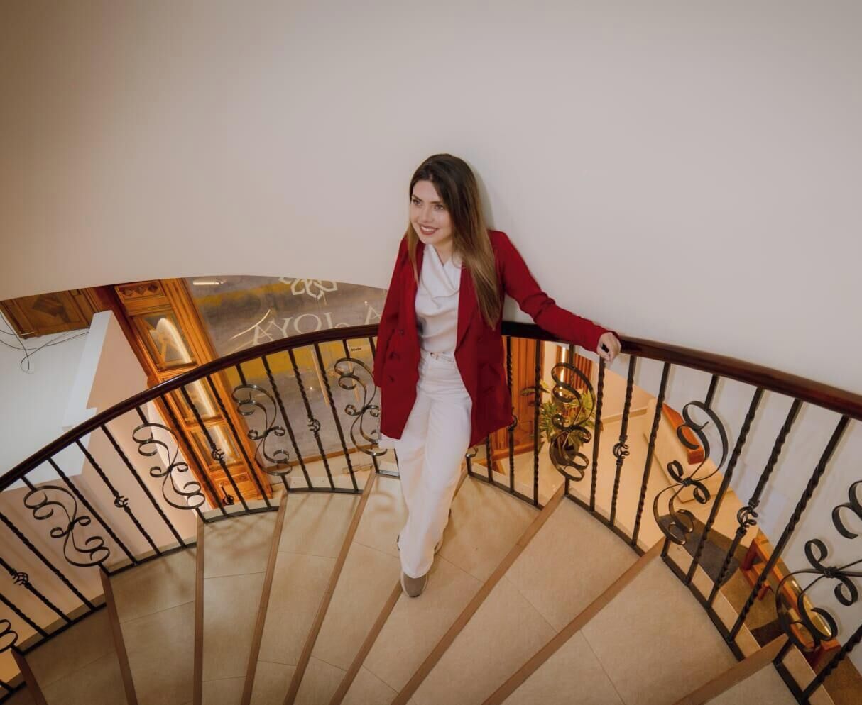 A person descending a curved staircase with ornate metal railings and a wooden handrail.