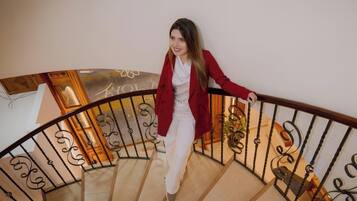 Una persona baja por una escalera curva con barandas de metal ornamentadas y un pasamanos de madera.