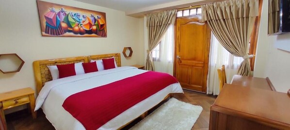 A bedroom with a large bed, a wooden headboard, a painting on the wall, and a wooden door. - HOTEL LA JOYA (Otavalo)
