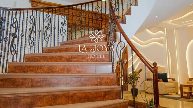 A staircase with a wooden handrail and metal balusters, leading to a landing with a seating area. - HOTEL LA JOYA (Otavalo)