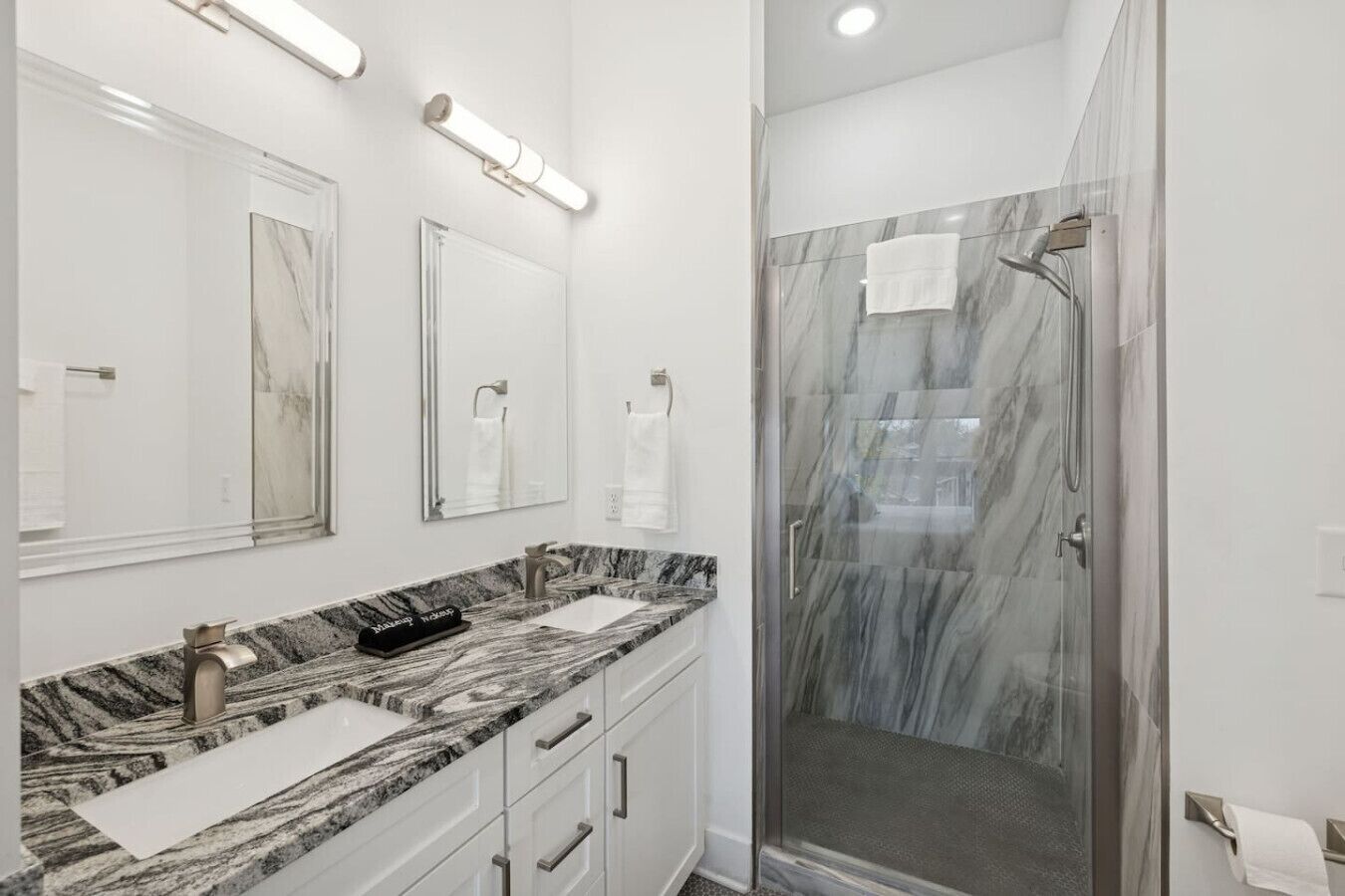 A modern bathroom with a marble vanity, two sinks, a shower with glass doors, and a large mirror.