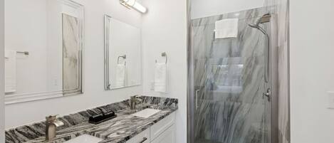 A modern bathroom with a marble vanity, two sinks, a shower with glass doors, and a large mirror.