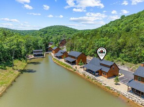 Eine Lodge am Flussufer mit mehreren Hütten, einer Steinbrücke und bewaldeter Landschaft im Hintergrund.