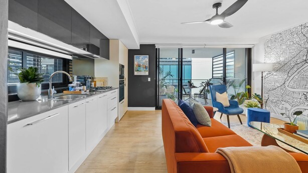 A modern kitchen with white cabinets, a dining area with a blue chair, and a large window. - 5min stroll to QPAC & Southbank with free parking (South Brisbane)